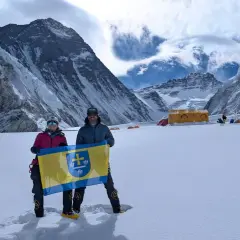 Polacy na Mount Everest dumnie prezentują flagę na tle majestatycznych gór. W tle widoczne namioty obozowe.