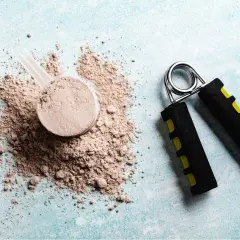 Miarka z proszkiem białkowym i przyrząd do ćwiczenia dłoni. Zastanawiasz się glutamine co to? To aminokwas wspierający regenerację.