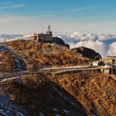 Kasprowy Wierch, gdzie jest szczyt Tatr, otoczony morzem chmur. Na zboczu widoczna kolejka i budynki.
