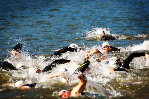 Zawodnicy walczą o pozycję podczas pływania na dystansie 1/2 ironman. Woda wzburzona, widać kaski i okulary.