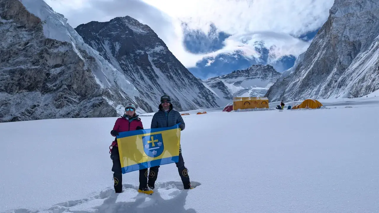 Polacy na Mount Everest dumnie prezentują flagę na tle majestatycznych gór. W tle widoczne namioty obozowe.