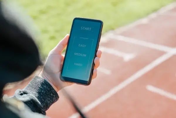 Dłoń trzyma smartfon z aplikacją "zacznij biegać". Wybierz poziom treningu: łatwy, średni lub trudny.